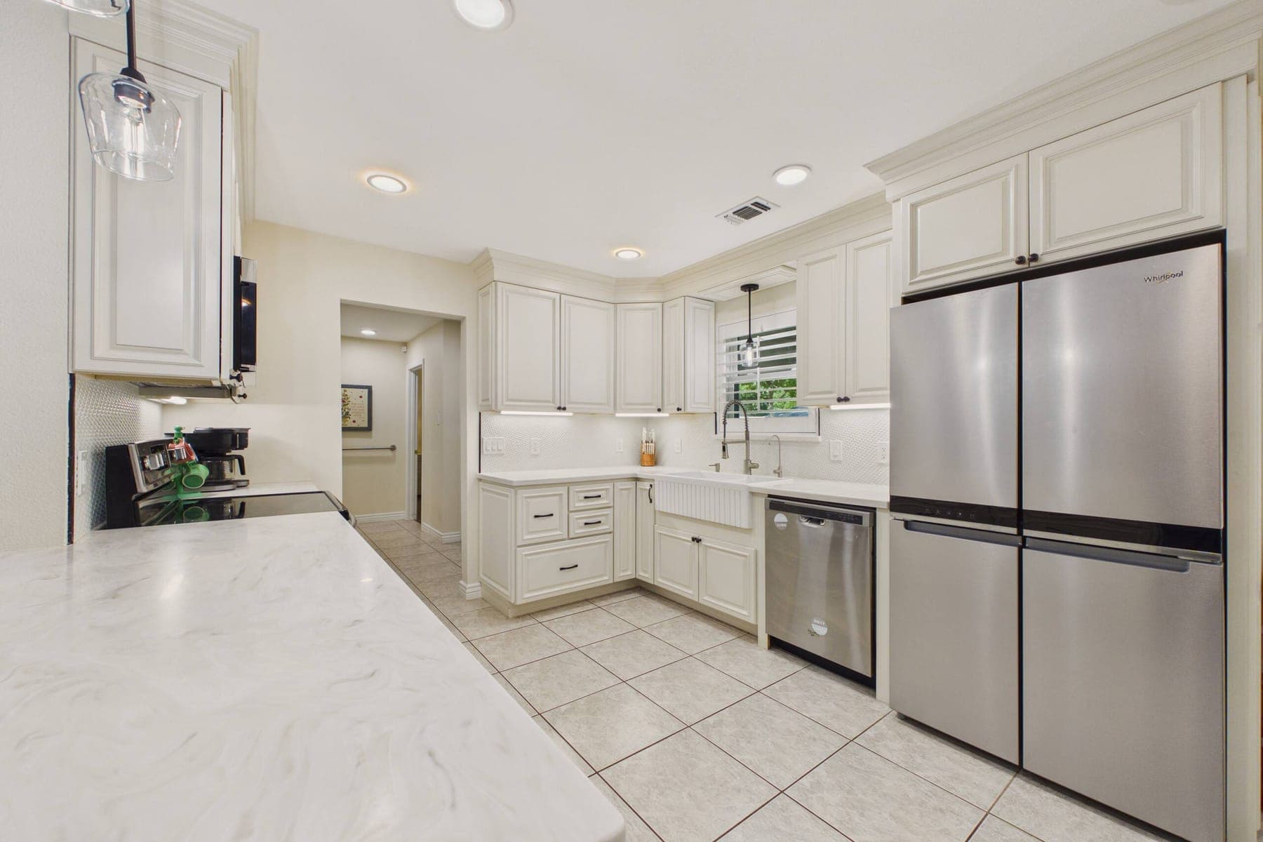 The remodeled kitchen: cream shaker cabinetry, marble-look quartz countertops, a farmhouse sink under the window, stainless appliances and tile flooring.